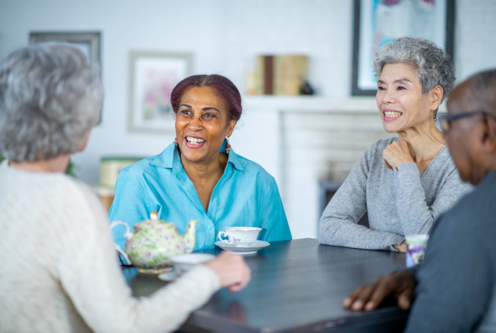 Seniors from different backgrounds and ages, sitting aroung a table having a conversation with a nurse and similing in a retirement home in Ontario